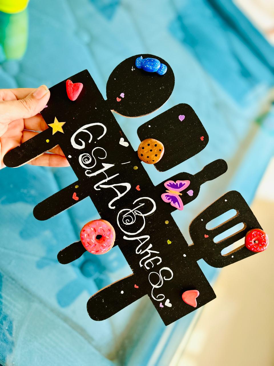 A hand-painted Whisk Away kitchen wall hanging held up by the artist